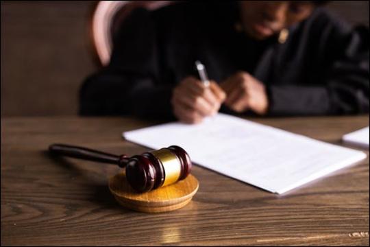 judge sitting at bench signing document with gavel on desk