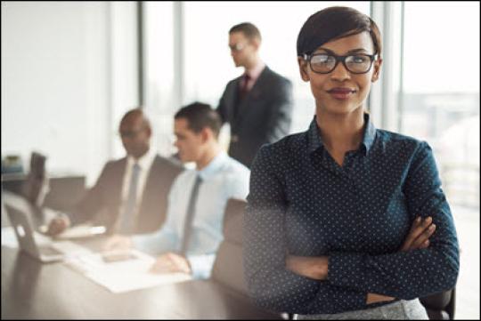 professional woman standing in front of conference desk where men are seated