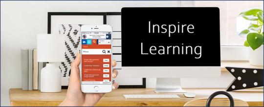 image of computer desk with words inspire learning on the screen and a hand holding up a mobile phone